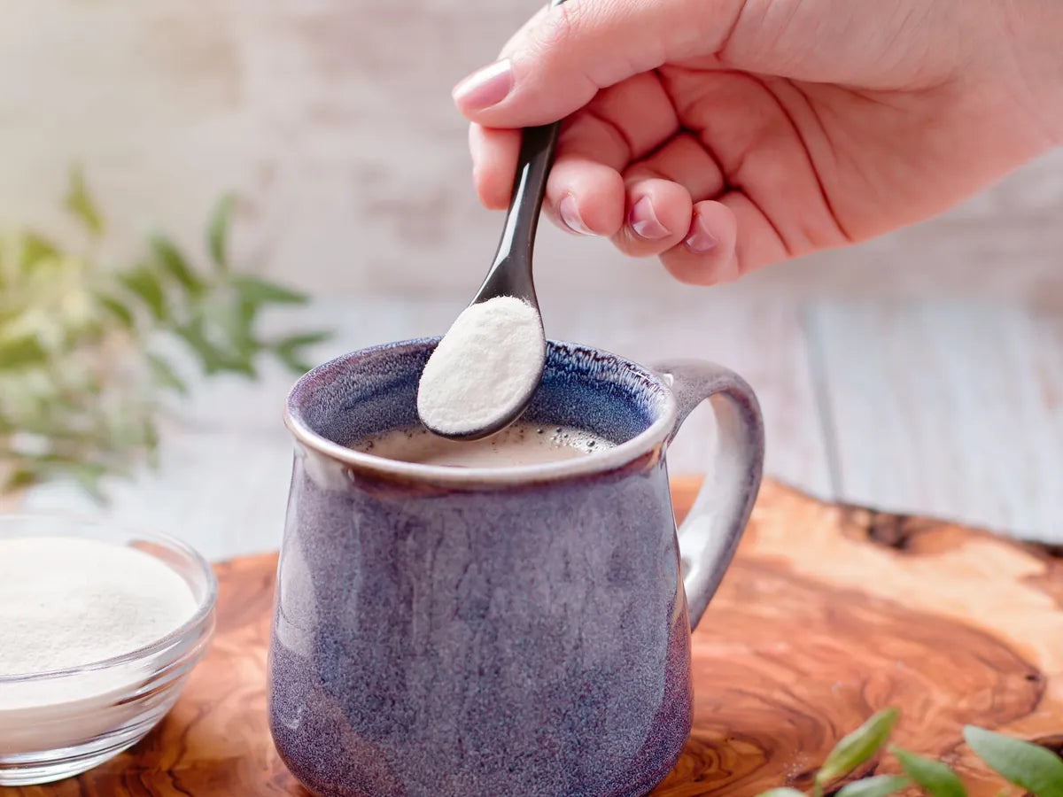 Eine Hand gibt Kollagenpulver mit einem Löffel in eine Tasse